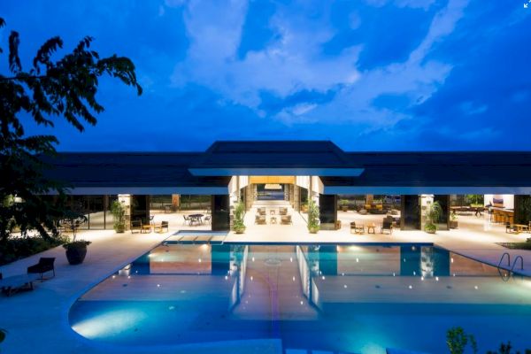 A luxurious, well-lit resort featuring a large swimming pool and outdoor seating areas under a twilight sky ending the sentence.