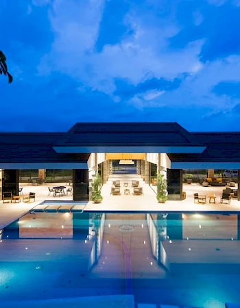 A luxurious resort with an illuminated swimming pool and lounge area under a dramatic evening sky.