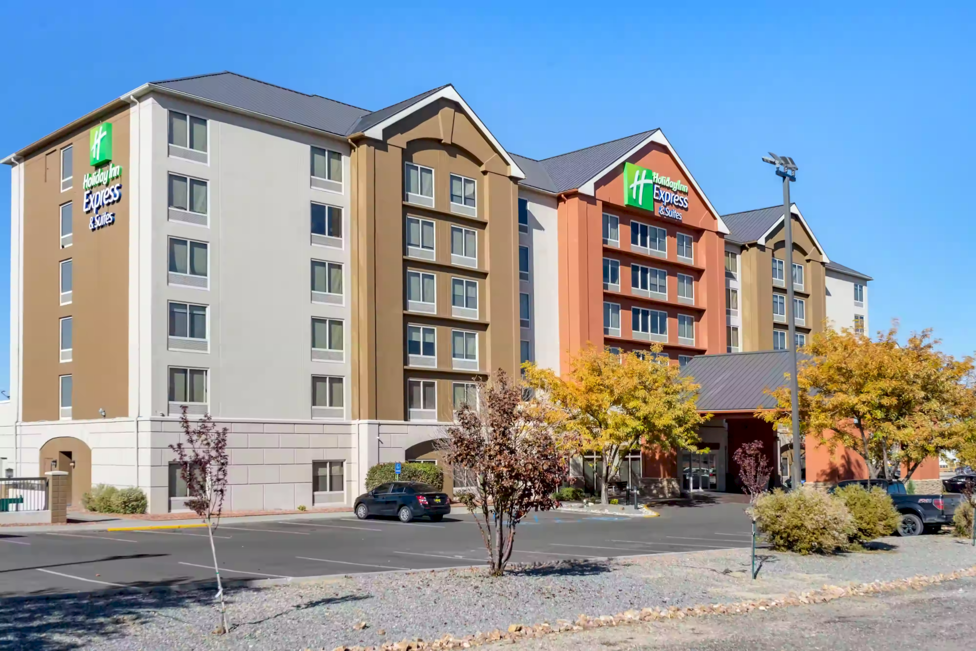 This image shows a multi-story Holiday Inn Express hotel with a parking lot and some autumn-colored trees in front of the building.