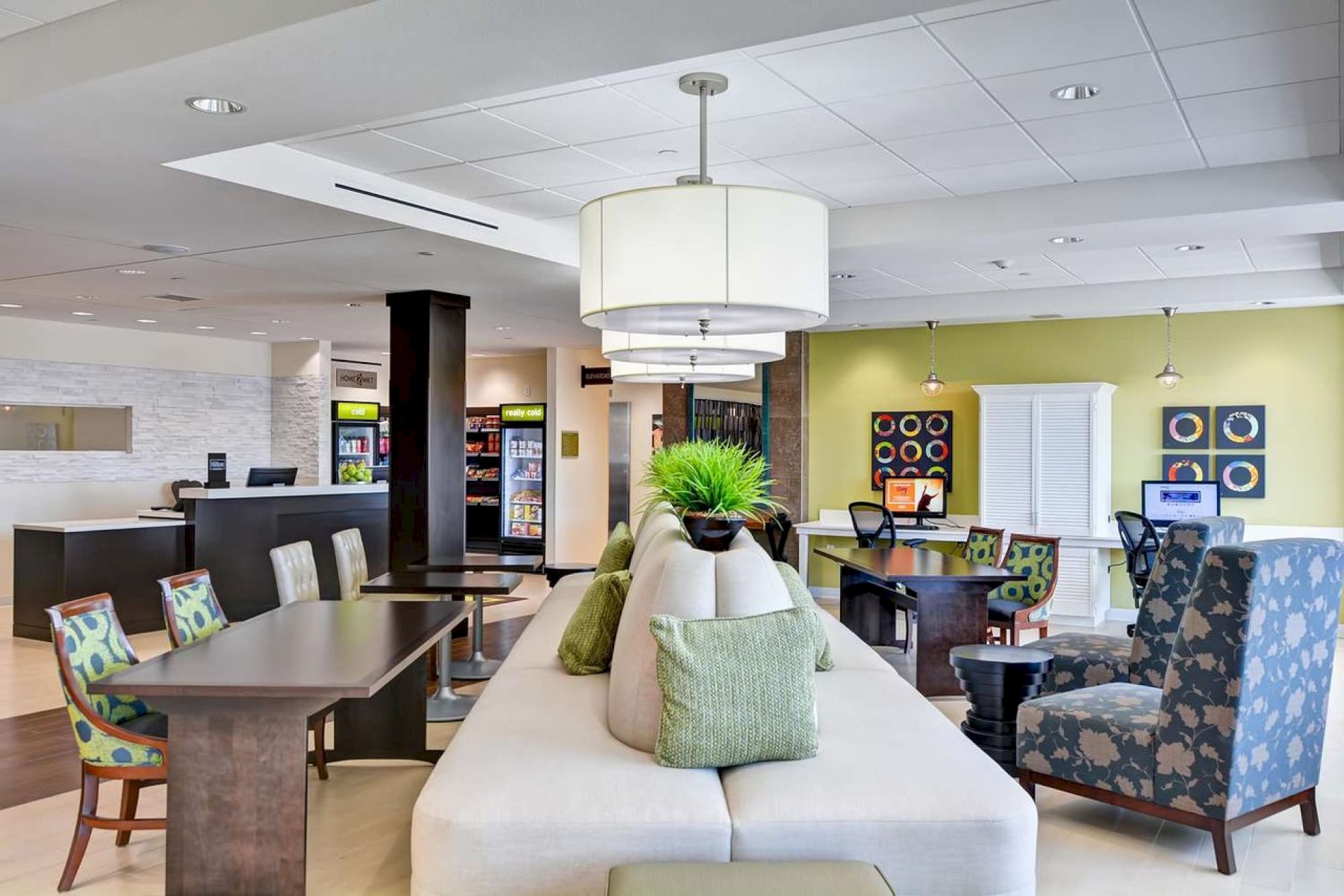 This image depicts a modern lounge area with comfortable seating, tables, plants, and colorful decor, suggesting a welcoming and stylish environment.