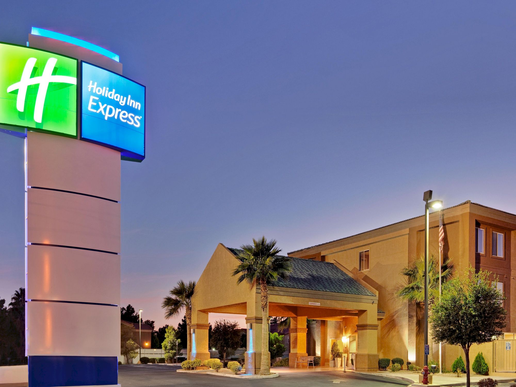 The image shows the exterior of a Holiday Inn Express hotel at dusk, with the hotel's sign prominently displayed and a well-lit entrance.