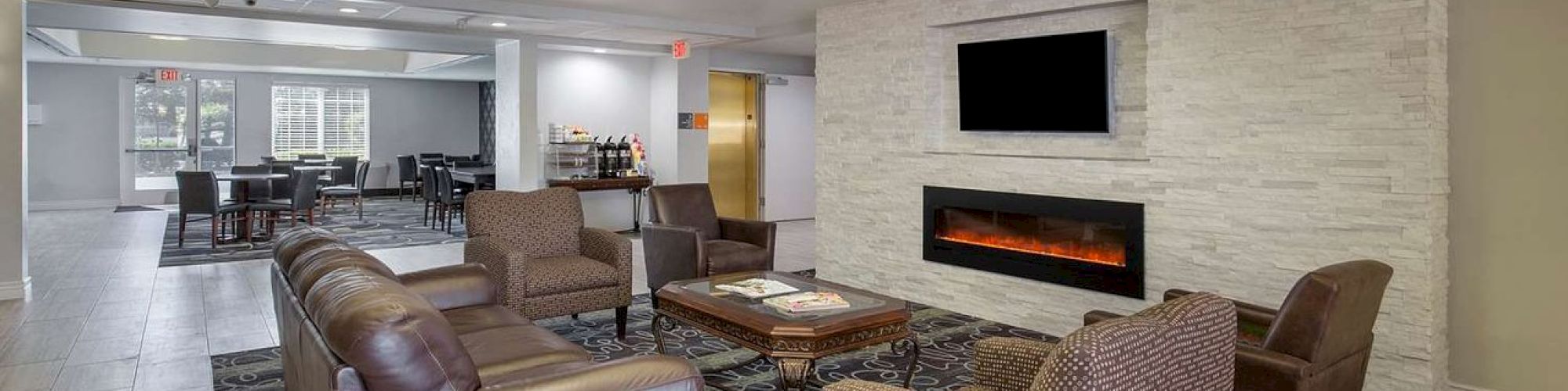 A modern living space with leather sofas, armchairs, a fireplace, wall-mounted TV, and a dining area in the background.