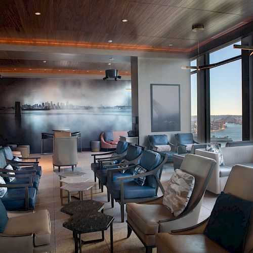 A cozy lounge with modern furniture, large windows offering ocean views, and a wall mural of a city skyline.