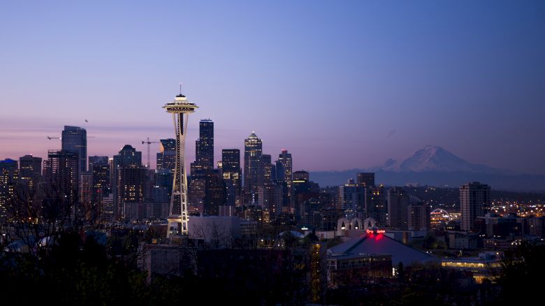 A cityscape at dusk featuring the Space Needle and downtown skyscrapers with a mountain in the background under a twilight sky.